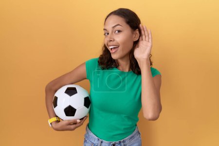 Téléchargez les photos : Jeune femme hispanique tenant le ballon souriant avec la main sur l'oreille en écoutant une rumeur ou des commérages. concept de surdité. - en image libre de droit
