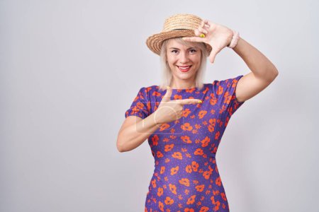 Foto de Young caucasian woman wearing flowers dress and summer hat smiling making frame with hands and fingers with happy face. creativity and photography concept. - Imagen libre de derechos