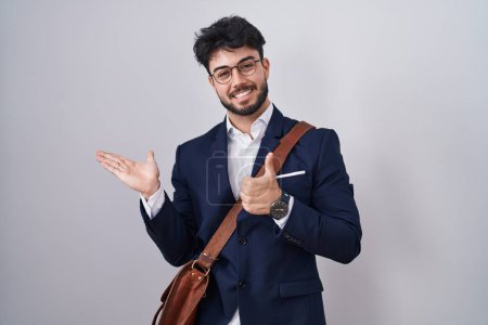 Foto de Hombre hispano con barba vistiendo ropa de negocios mostrando la palma de la mano y haciendo buen gesto con los pulgares hacia arriba, sonriendo feliz y alegre - Imagen libre de derechos