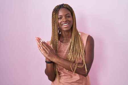 Téléchargez les photos : Femme afro-américaine avec les cheveux tressés debout sur fond rose applaudissements heureux et joyeux, souriant mains fières ensemble - en image libre de droit