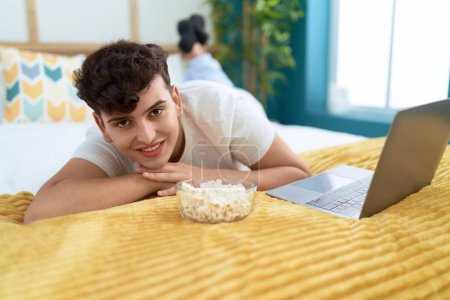 Téléchargez les photos : Homme non binaire regardant un film sur ordinateur portable couché sur le lit dans la chambre - en image libre de droit