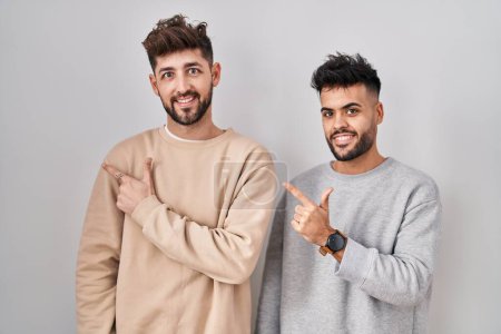 Téléchargez les photos : Young homosexual couple standing over white background cheerful with a smile on face pointing with hand and finger up to the side with happy and natural expression - en image libre de droit