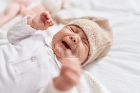 Téléchargez les photos : Adorable bébé hispanique couché sur le lit pleurant dans la chambre - en image libre de droit