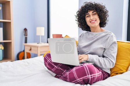 Téléchargez les photos : Young middle east woman using laptop drinking coffee sitting on bed at bedroom - en image libre de droit
