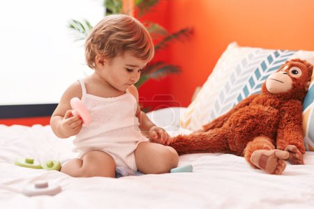 Téléchargez les photos : Adorable bambin hispanique jouant avec jouet assis sur le lit dans la chambre - en image libre de droit