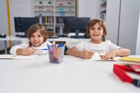 Photo for Brother and sister students writing on notebook studying at classroom - Royalty Free Image