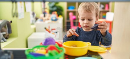 Téléchargez les photos : Adorable tout-petit blond jouant avec la cuisine de jeu debout à la maternelle - en image libre de droit