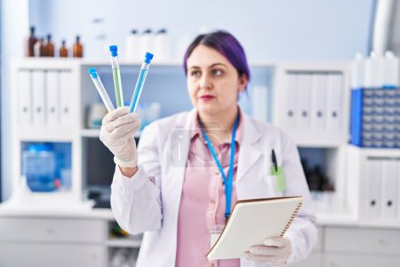 Téléchargez les photos : Young beautiful plus size woman scientist reading notebook holding test tubes at laboratory - en image libre de droit