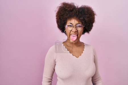 Téléchargez les photos : Jeune femme afro-américaine debout sur fond rose langue collante heureux avec une expression drôle. concept d'émotion. - en image libre de droit