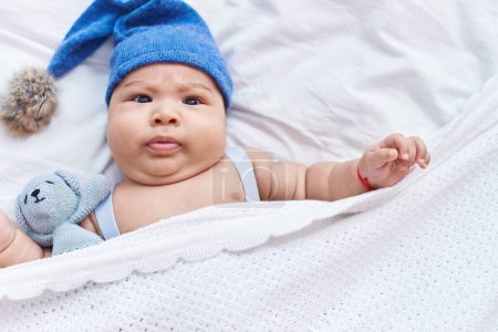 Téléchargez les photos : Adorable bambin hispanique portant une casquette en laine couchée sur le lit dans la chambre - en image libre de droit