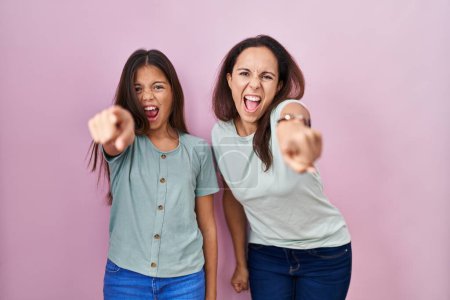 Foto de Young mother and daughter standing over pink background pointing displeased and frustrated to the camera, angry and furious with you - Imagen libre de derechos