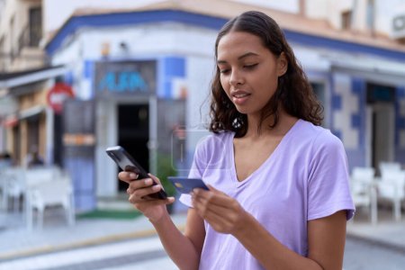 Téléchargez les photos : Jeune femme afro-américaine utilisant smartphone et carte de crédit à la terrasse du café - en image libre de droit