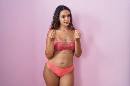 Photo for Young hispanic woman wearing lingerie over pink background doing money gesture with hands, asking for salary payment, millionaire business - Royalty Free Image