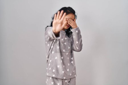 Téléchargez les photos : Young asian woman wearing pajama covering eyes with hands and doing stop gesture with sad and fear expression. embarrassed and negative concept. - en image libre de droit