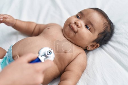 Foto de Bebé afroamericano sonriendo confiado teniendo examen médico en el dormitorio - Imagen libre de derechos