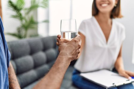 Téléchargez les photos : Homme et femme ayant séance de psychologie donnant un verre d'eau à la clinique de psychologie - en image libre de droit