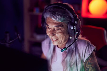 Téléchargez les photos : Moyen âge femme aux cheveux gris streamer jouer à un jeu vidéo en utilisant l'ordinateur à la salle de jeux - en image libre de droit