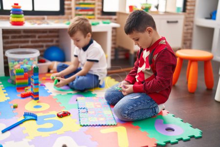 Foto de Dos niños jugando con bloques de construcción y matemáticas juego de puzzle sentado en el suelo en el jardín de infantes - Imagen libre de derechos