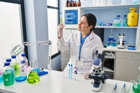 Téléchargez les photos : Jeune femme hispanique portant l'uniforme scientifique tenant le tube à essai au laboratoire - en image libre de droit