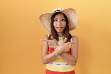 Téléchargez les photos : Femme chinoise du Moyen Âge portant un chapeau d'été sur fond jaune pointant des deux côtés avec les doigts, direction différente en désaccord - en image libre de droit