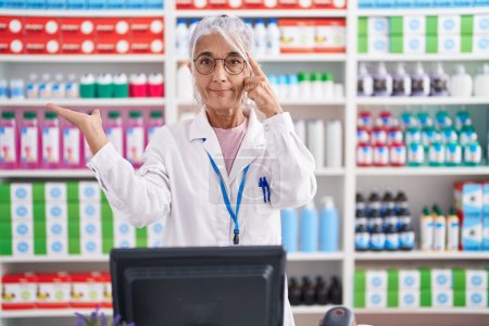 Photo for Middle age woman with tattoos working at pharmacy drugstore confused and annoyed with open palm showing copy space and pointing finger to forehead. think about it. - Royalty Free Image