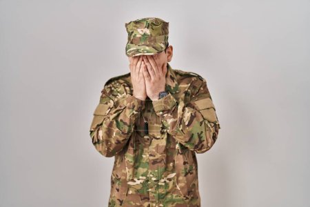 Foto de Joven árabe vestido con camuflaje uniforme del ejército con expresión triste cubriendo la cara con las manos mientras llora. concepto de depresión. - Imagen libre de derechos