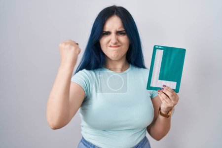 Téléchargez les photos : Young modern girl with blue hair holding l sign for new driver annoyed and frustrated shouting with anger, yelling crazy with anger and hand raised - en image libre de droit