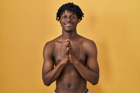 Photo for Young african man with dreadlocks standing shirtless praying with hands together asking for forgiveness smiling confident. - Royalty Free Image