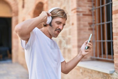 Téléchargez les photos : Jeune homme blond écoutant de la musique et dansant dans la rue - en image libre de droit
