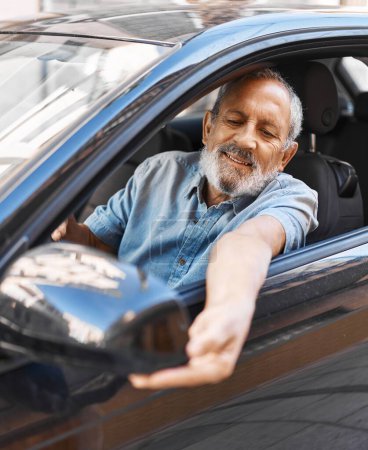 Photo for Senior grey-haired man touching rearview sitting on car at street - Royalty Free Image