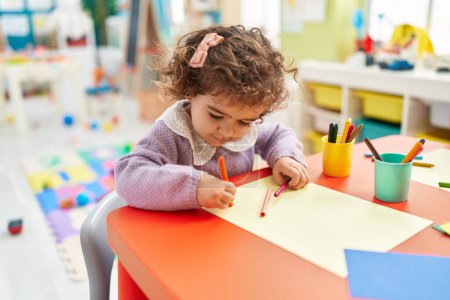 Photo for Adorable hispanic girl preschool student sitting on table drawing on paper at kindergarten - Royalty Free Image