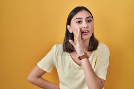 Photo for Hispanic girl wearing casual t shirt over yellow background hand on mouth telling secret rumor, whispering malicious talk conversation - Royalty Free Image