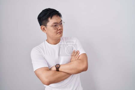 Foto de Young asian man standing over white background looking to the side with arms crossed convinced and confident - Imagen libre de derechos