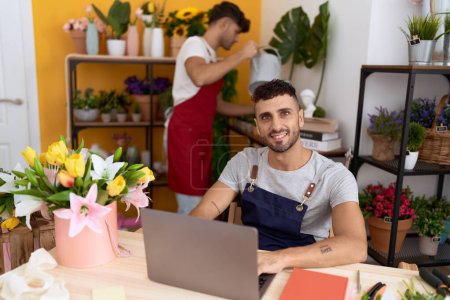 Téléchargez les photos : Two hispanic men florists using laptop and touchpad working at flower shop - en image libre de droit