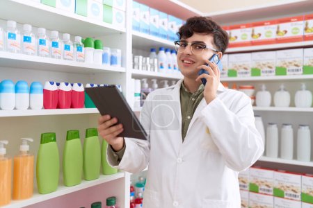 Foto de Non binary man pharmacist using touchpad talking on smartphone at pharmacy - Imagen libre de derechos
