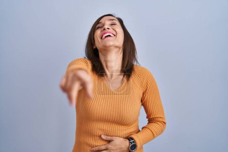 Foto de Mujer morena de mediana edad de pie con suéter naranja riéndose de ti, señalando con el dedo a la cámara con la mano sobre el cuerpo, expresión de vergüenza - Imagen libre de derechos