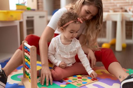 Photo for Teacher and toddler playing with maths puzzle game sitting on floor at kindergarten - Royalty Free Image