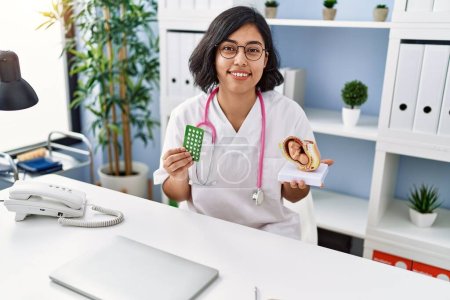 Photo for Young hispanic doctor woman holding anatomical model of uterus with fetus and birth control pills smiling with a happy and cool smile on face. showing teeth. - Royalty Free Image