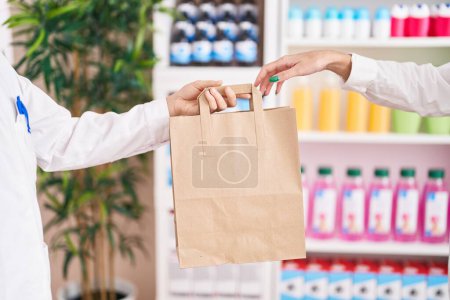 Foto de Young beautiful hispanic woman customer holding shopping bag of pharmacist at pharmacy - Imagen libre de derechos