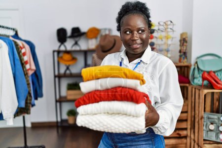 Foto de Young african american woman shopkeeper smiling confident holding folded clothes at clothing store - Imagen libre de derechos