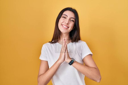 Photo for Young beautiful woman standing over yellow background praying with hands together asking for forgiveness smiling confident. - Royalty Free Image