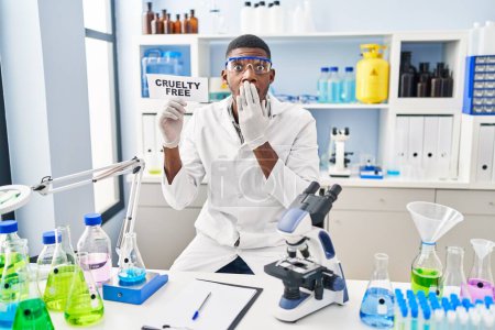 Foto de African american man working on cruelty free laboratory covering mouth with hand, shocked and afraid for mistake. surprised expression - Imagen libre de derechos