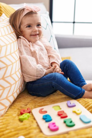 Foto de Adorable niño rubio jugando con las matemáticas juego de puzzle sentado en el sofá en casa - Imagen libre de derechos