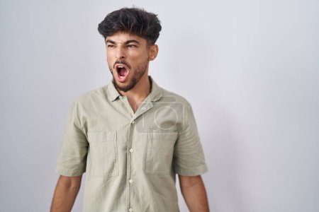 Téléchargez les photos : Arab man with beard standing over white background angry and mad screaming frustrated and furious, shouting with anger. rage and aggressive concept. - en image libre de droit