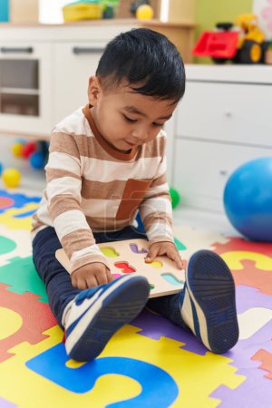 Téléchargez les photos : Adorable bambin hispanique jouer avec des mathématiques jeu de puzzle assis sur le sol à la maternelle - en image libre de droit