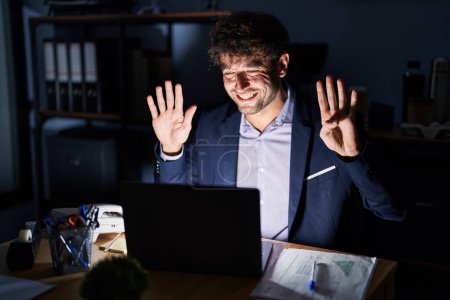 Téléchargez les photos : Hispanic young man working at the office at night showing and pointing up with fingers number nine while smiling confident and happy. - en image libre de droit