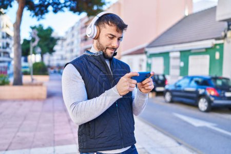 Photo for Young hispanic man smiling confident playing video game at street - Royalty Free Image