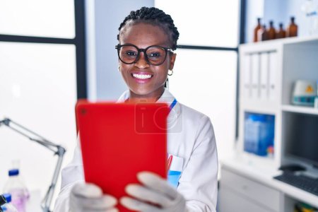 Foto de African american woman scientist smiling confident using touchpad at laboratory - Imagen libre de derechos