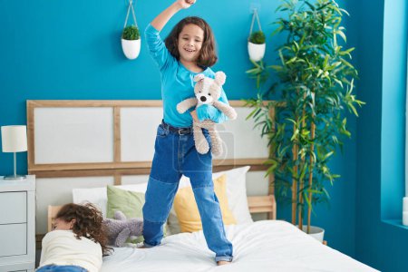 Photo for Two kids holding teddy bear dancing on bed at bedroom - Royalty Free Image