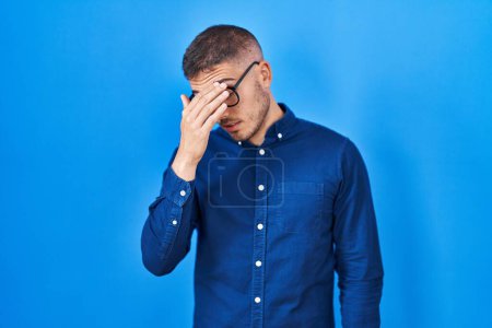 Photo for Young hispanic man wearing glasses over blue background tired rubbing nose and eyes feeling fatigue and headache. stress and frustration concept. - Royalty Free Image